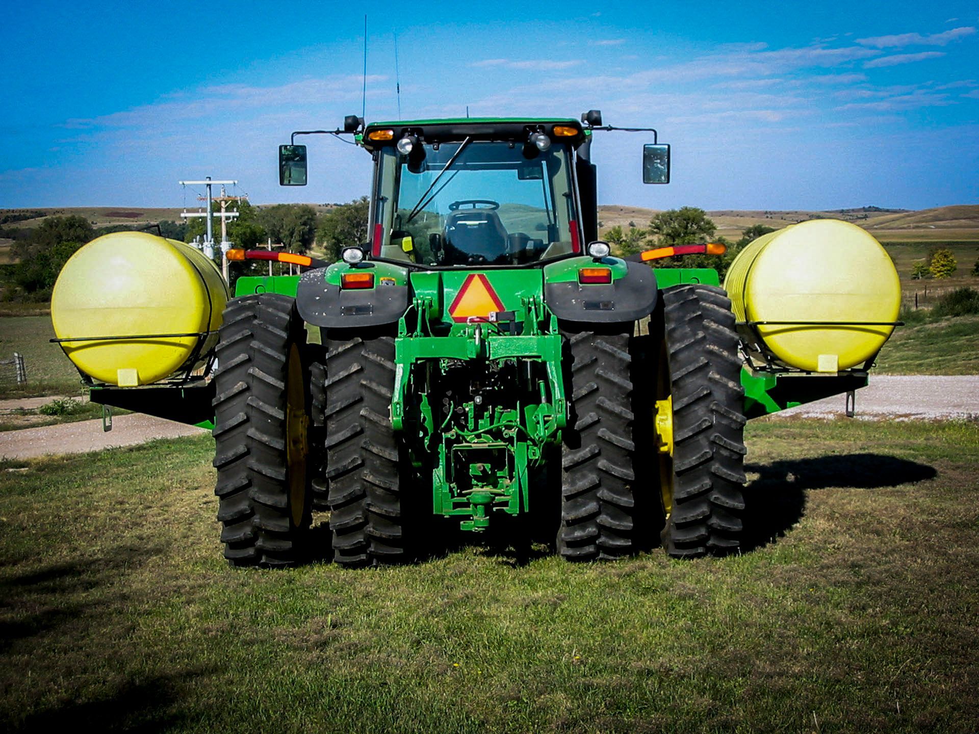 A green tractor with two yellow barrels attached to it is parked in a grassy field.