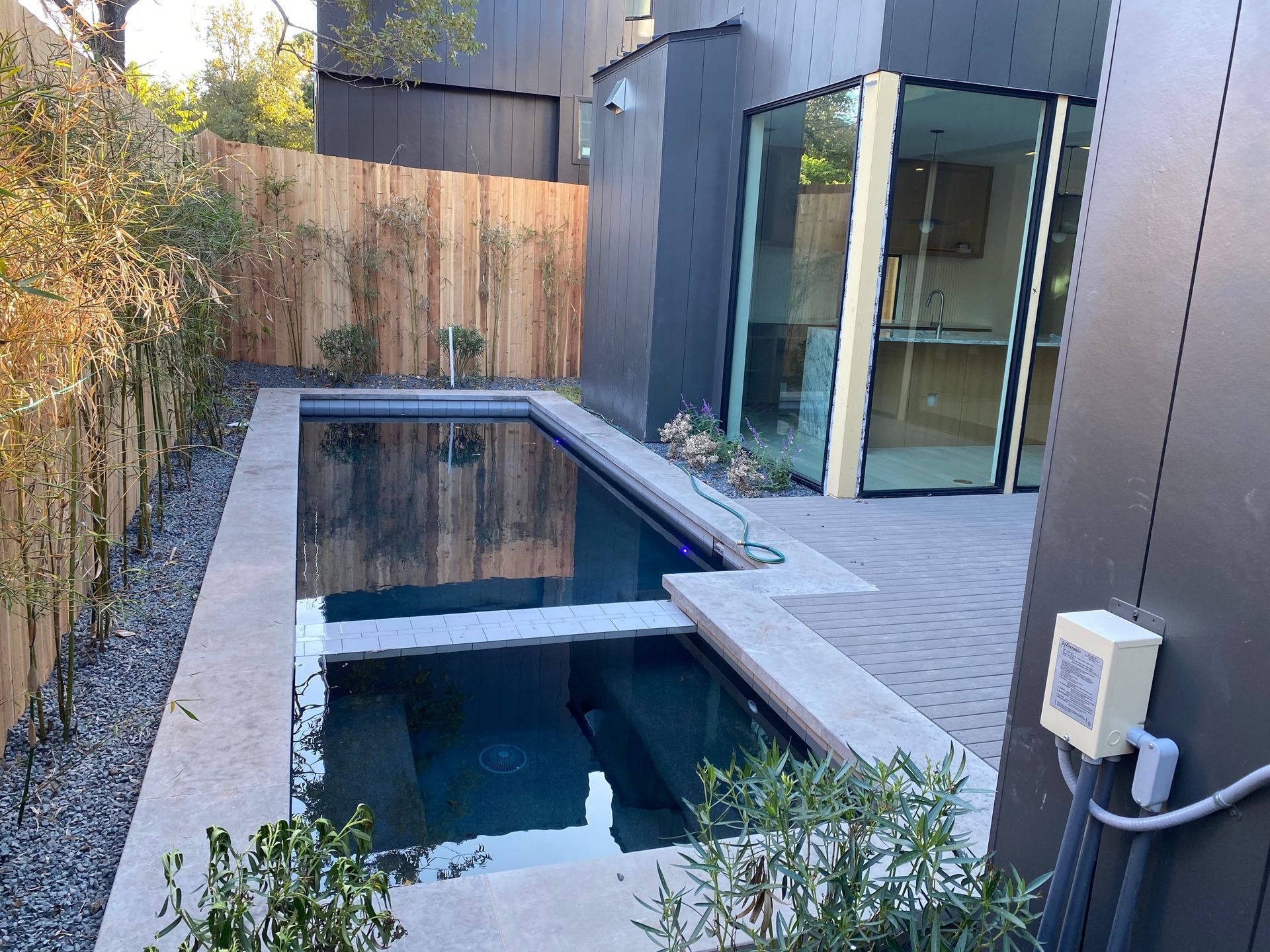 Modern backyard with a small rectangular plunge pool, gray decking, and glass sliding doors.