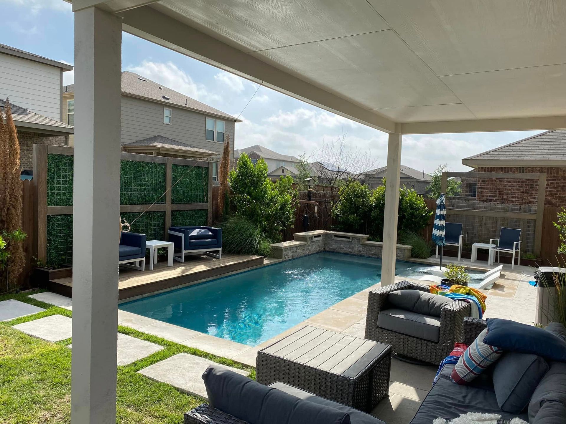 Covered backyard patio with a swimming pool, lounge chairs, and a small dining area beside a garden path.