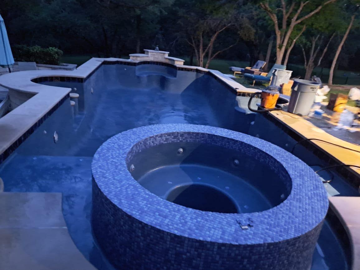 Backyard pool at dusk with a circular spa in the foreground and landscaping lights along the deck
