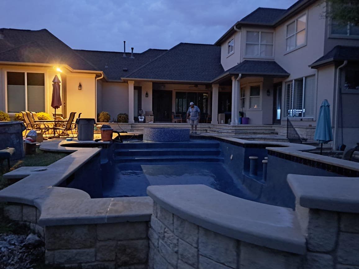 Backyard pool and spa at dusk beside a modern house, with patio lights glowing.
