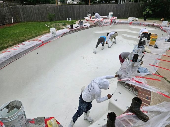 Workers resurfacing an empty swimming pool with white coating and red tape around the edge