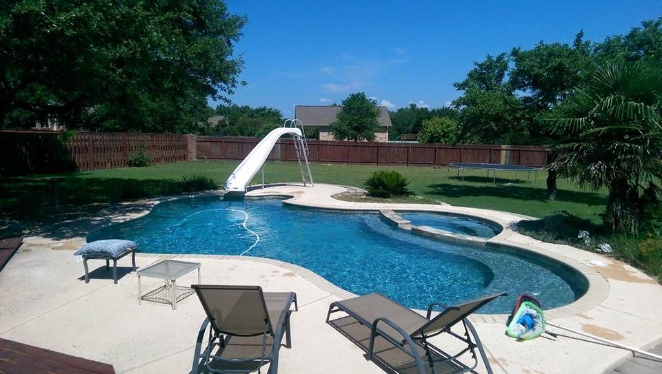 Backyard swimming pool with waterfall, patio chairs, and brick privacy wall surrounded by trees