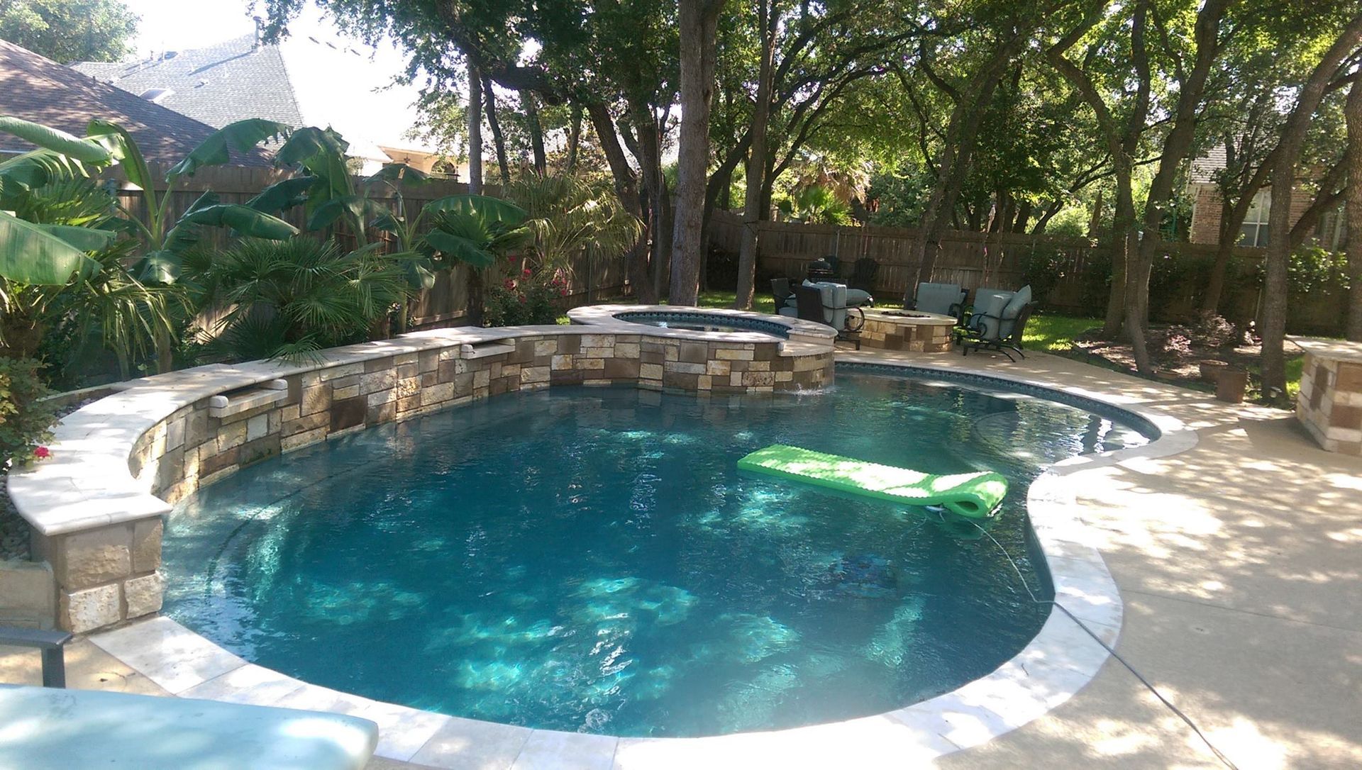 Backyard pool with stone waterfall, surrounded by trees and patio seating