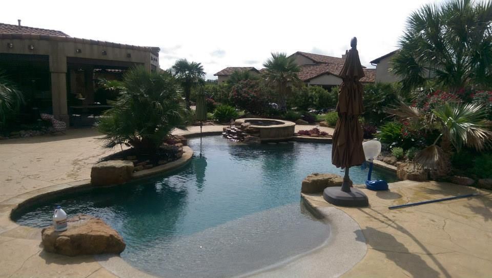 Resort pool with curved blue water, stone islands, umbrellas, and lounge chairs beside tropical greenery