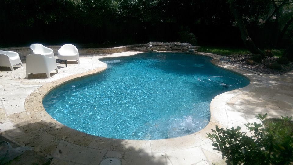 Backyard swimming pool with turquoise water, white lounge chairs, and stone patio surrounded by greenery