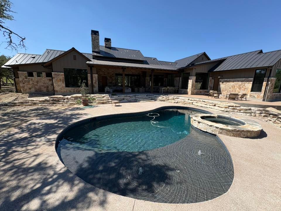 Stone house patio with a swimming pool and hot tub in a sunny backyard