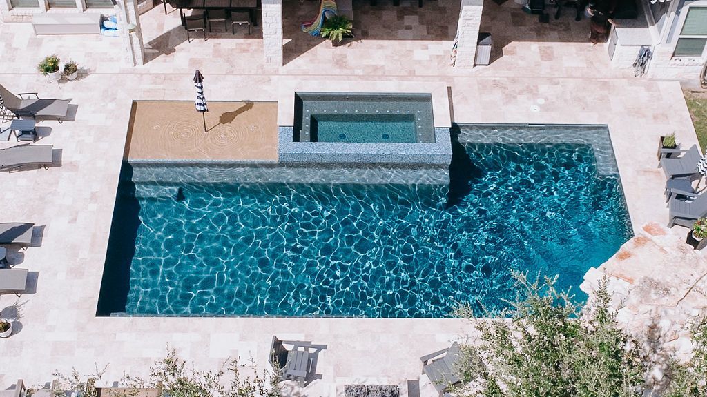 Blue swimming pool with a raised spa and lounge chairs on a sunny resort patio
