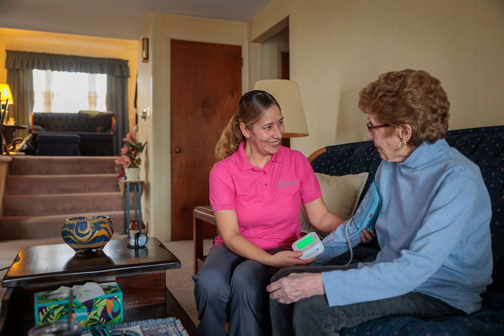 A caregiver is giving an elderly woman a glass of water.
