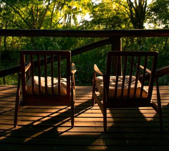Dos sillas de madera con cojines están situadas en una terraza, con vistas al bosque al fondo.