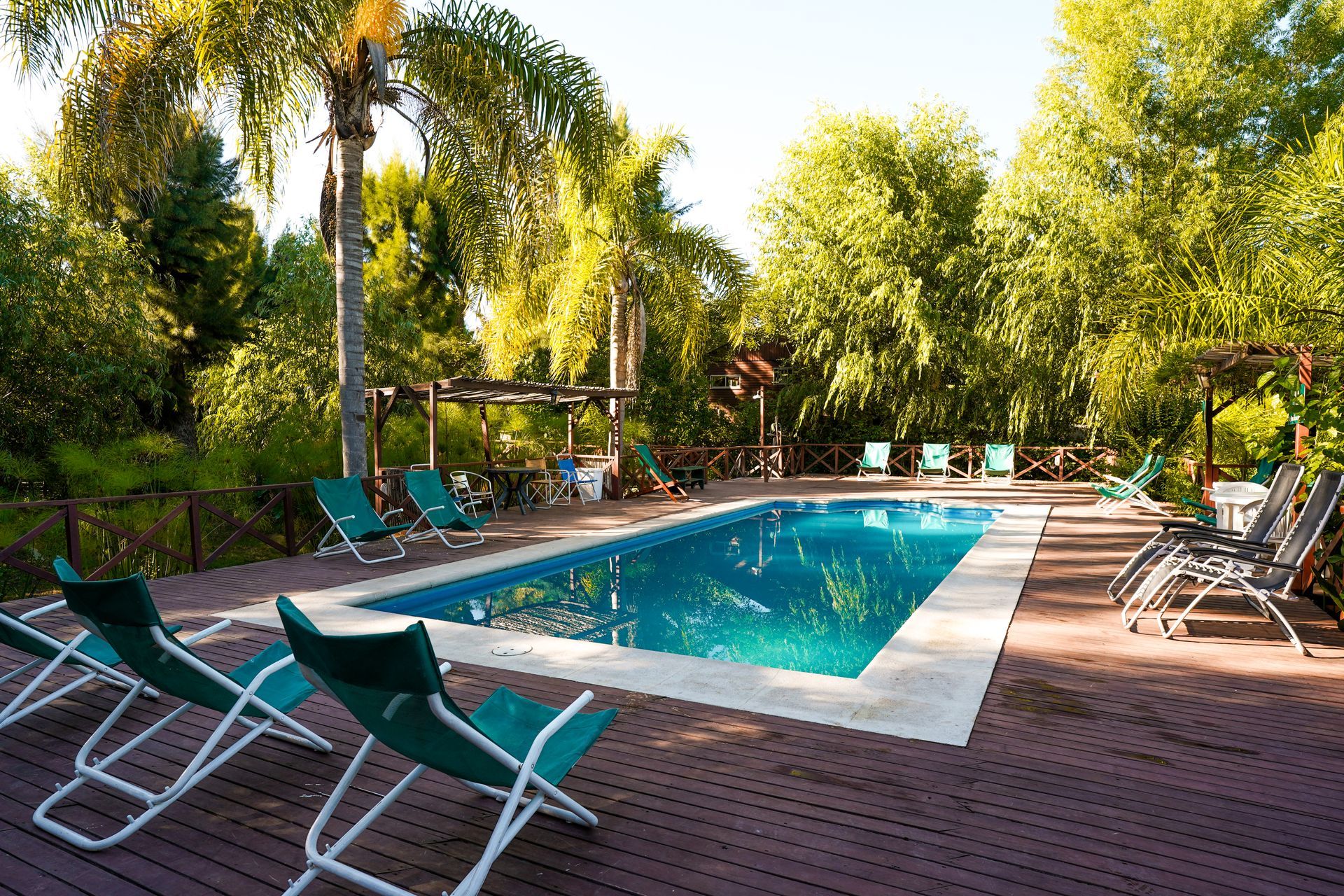 Piscina rodeada de sillas verdes y árboles sobre una terraza de madera.