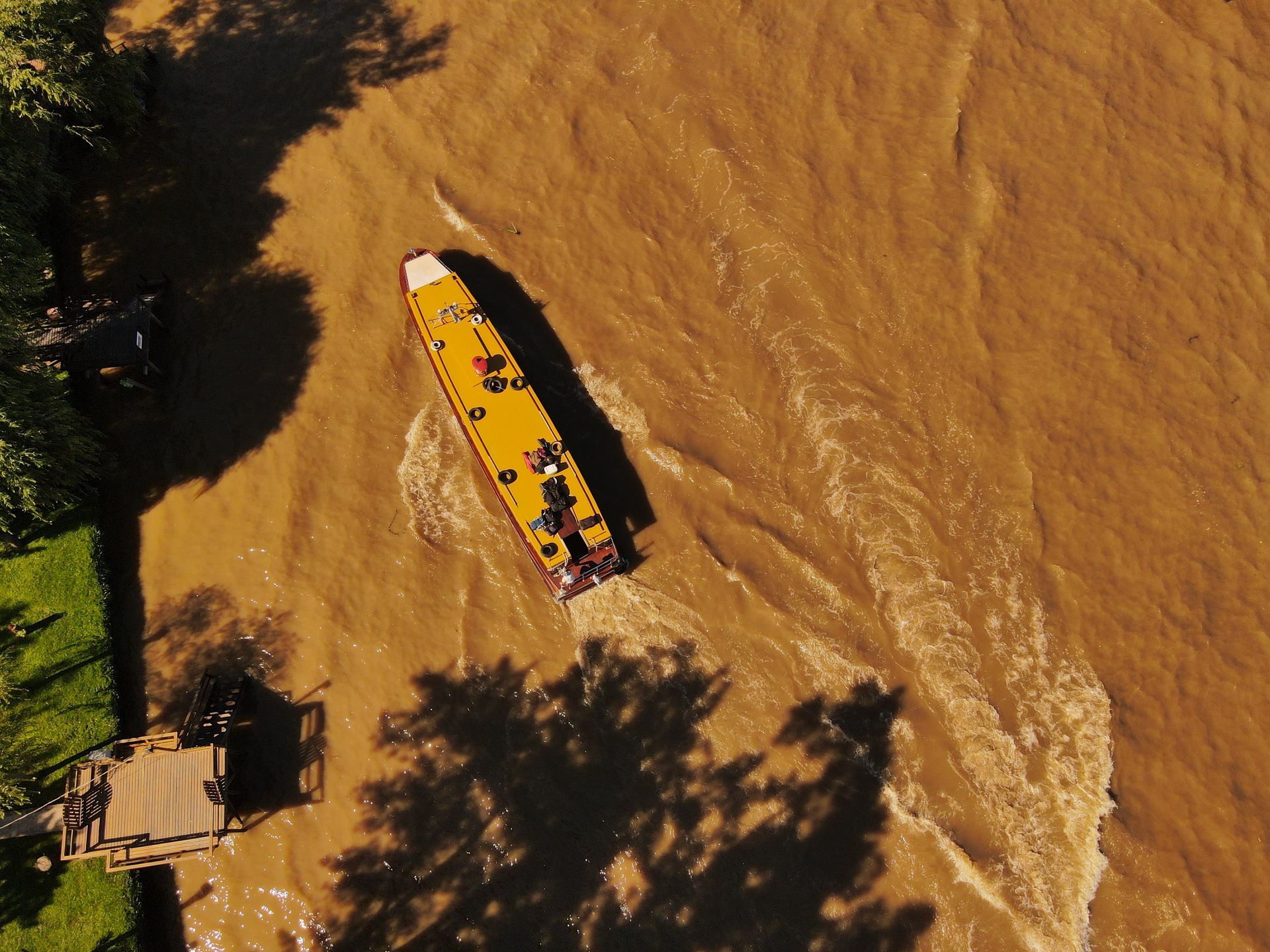 Un bote amarillo en un río marrón fangoso junto a una orilla cubierta de hierba con un pequeño muelle de madera.