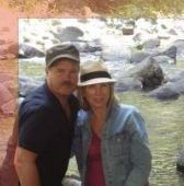 A man and a woman are posing for a picture in front of a river.