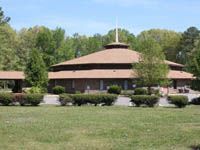 A church with a cross on top of it is surrounded by trees and grass.