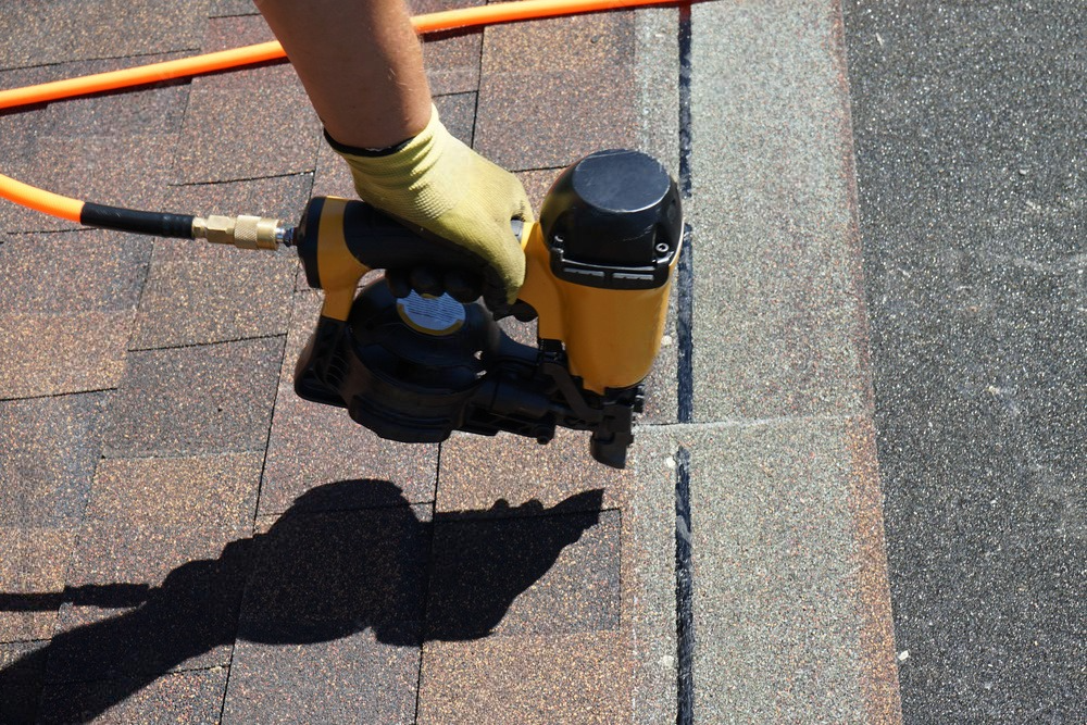 Construction worker putting the asphalt roofing with nail gun