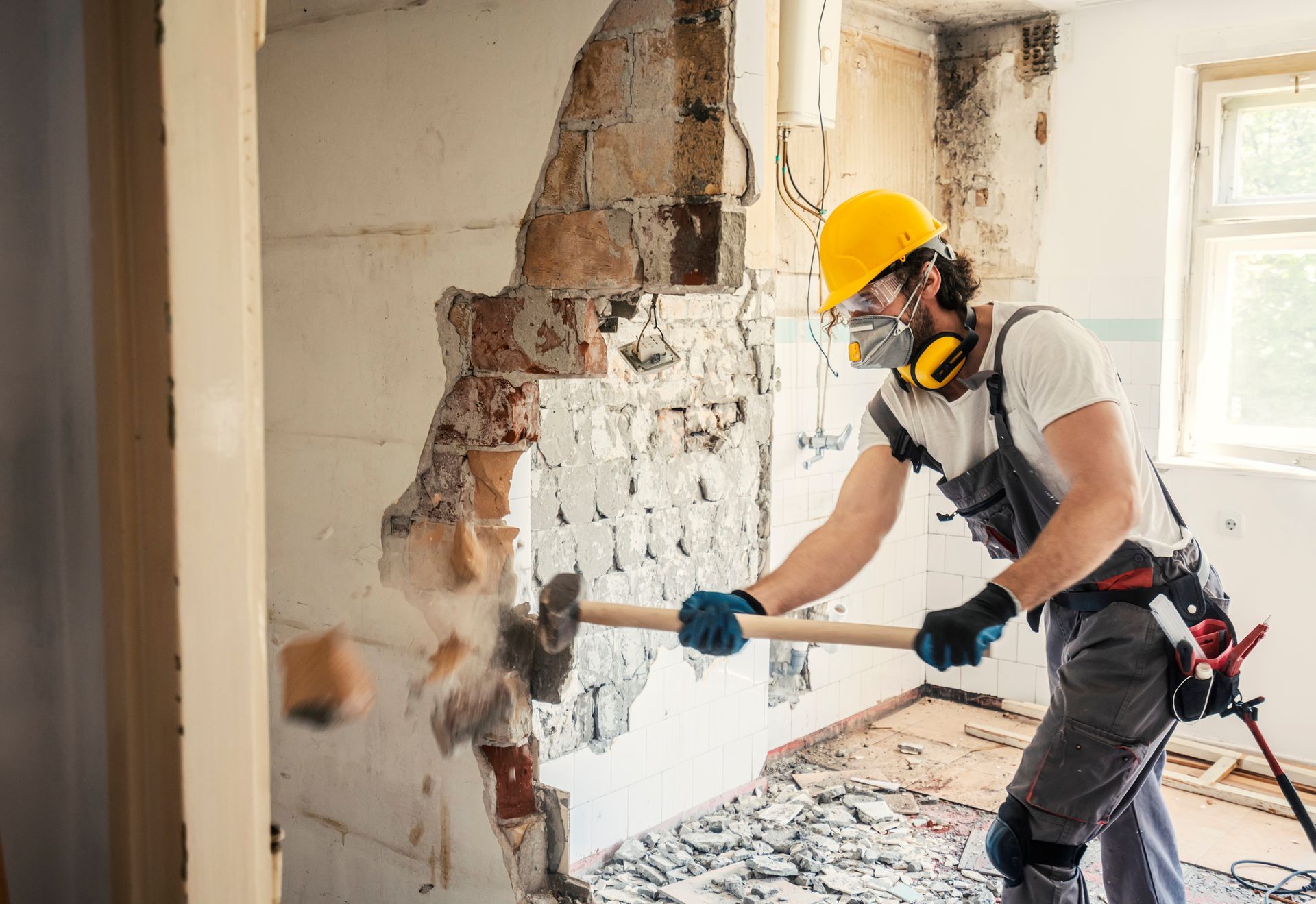 Worker in safety gear demolishing wall with sledgehammer in a renovated room.