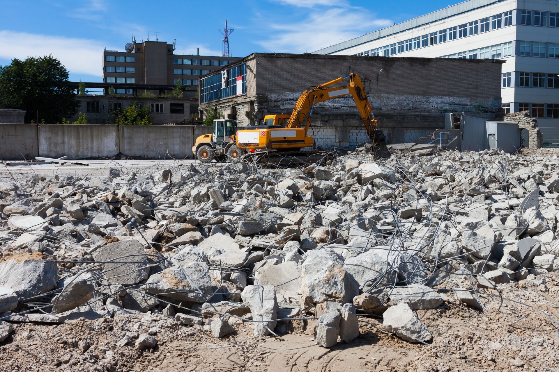 An orange digger demolishes houses for reconstruction, with rubble on the ground.