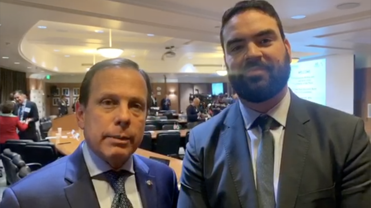 Two men in suits posing for a photo in a conference room; one with beard.