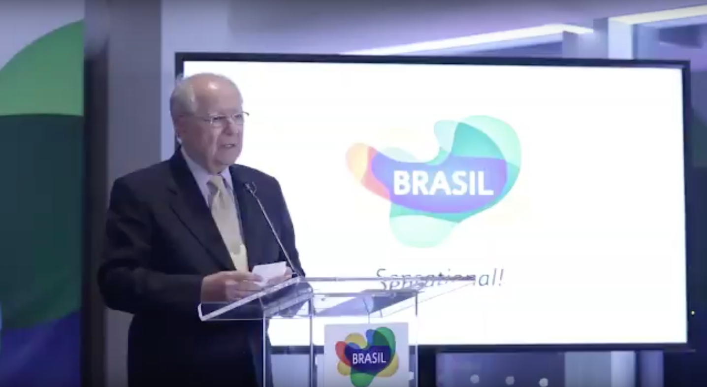 Man in suit speaking at a podium in front of a screen with