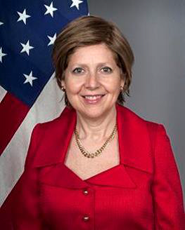 Official portrait of Elena Kagan, U.S. Ambassador to the United Nations. She wears a red suit, smiles, and stands before the American flag.