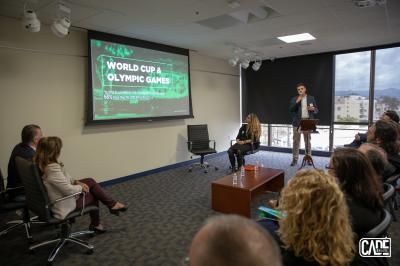 Man speaking at a podium in a room during a presentation about the World Cup & Olympic Games.