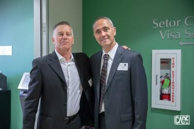 Two men in suits posing together near a sign that says 