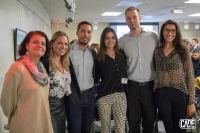 Group of six people posing for a photo indoors; white walls, neutral colors.