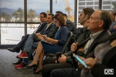 People seated in an office, looking towards a window. Some are holding phones or papers, focused.