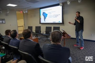 Man giving a presentation to a seated audience, South America map on screen.
