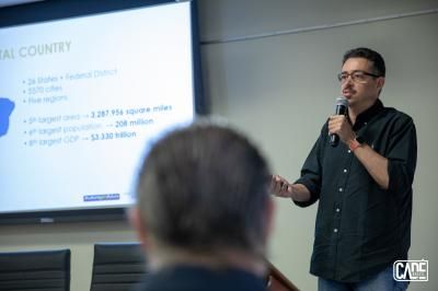 Man giving a presentation, standing in front of a screen with statistics, holding a microphone.