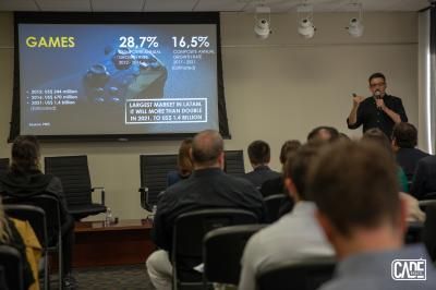 A man presents data to an audience; a projection screen shows statistics on the gaming market.