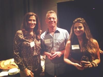 Three people smiling, at an event. Man in center, flanked by two women. All are wearing name tags.