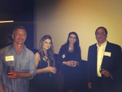 Four people at an event, smiling. Two men and two women, wearing business casual attire, holding drinks.