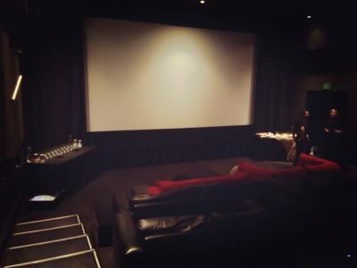 A dimly lit screening room with a large screen and black seating.