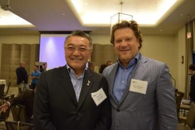 Two men smiling, posing for a photo in a conference room. One is Asian, the other is white.