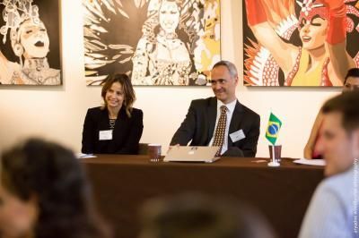 Woman and man smiling at a table. Brazilian flag and colorful art pieces in the background.