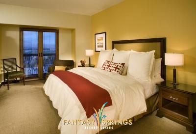 Cozy hotel bedroom with a king-size bed, red runner, and a door to a balcony; walls are yellow.