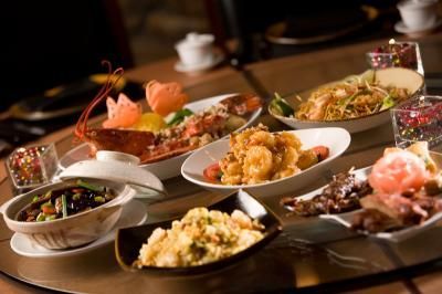 Several Asian dishes on a wooden table, including lobster, noodles, and rice.