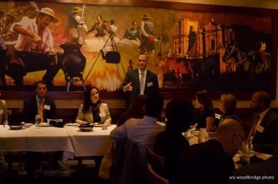 A panel discussion at a restaurant. A man speaks, others sit at a table in front of a mural.
