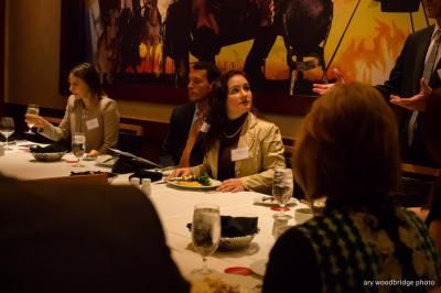 People at a formal dinner table, some looking up. Dark room with artwork on wall.