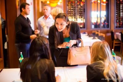 Woman in business attire smiles at seated women at a table, in a restaurant setting.