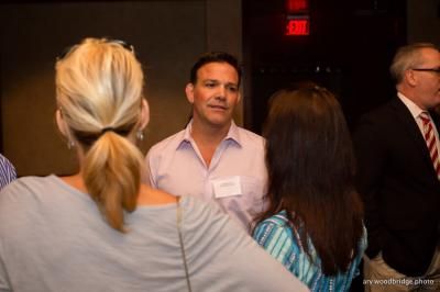 People conversing at an event. A man in a light pink shirt speaks with two women. Others stand nearby.