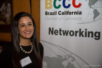 Woman smiling, stands by a BCCC networking banner, Brazil California Chamber of Commerce.