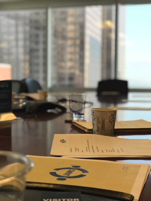 Conference table with papers, a cup, and a glass, with blurred city buildings in the background.