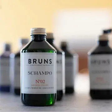 Een fles Bruns Champo No. 2 staat centraal op een tafel, met twee wazige flessen op de achtergrond.