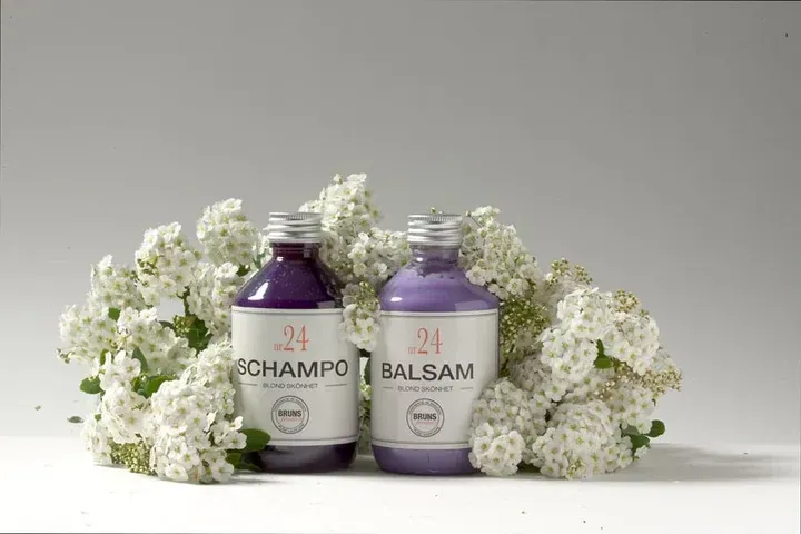 Twee paarse shampoo- en balsemflessen met witte bloemen op een lichte achtergrond.