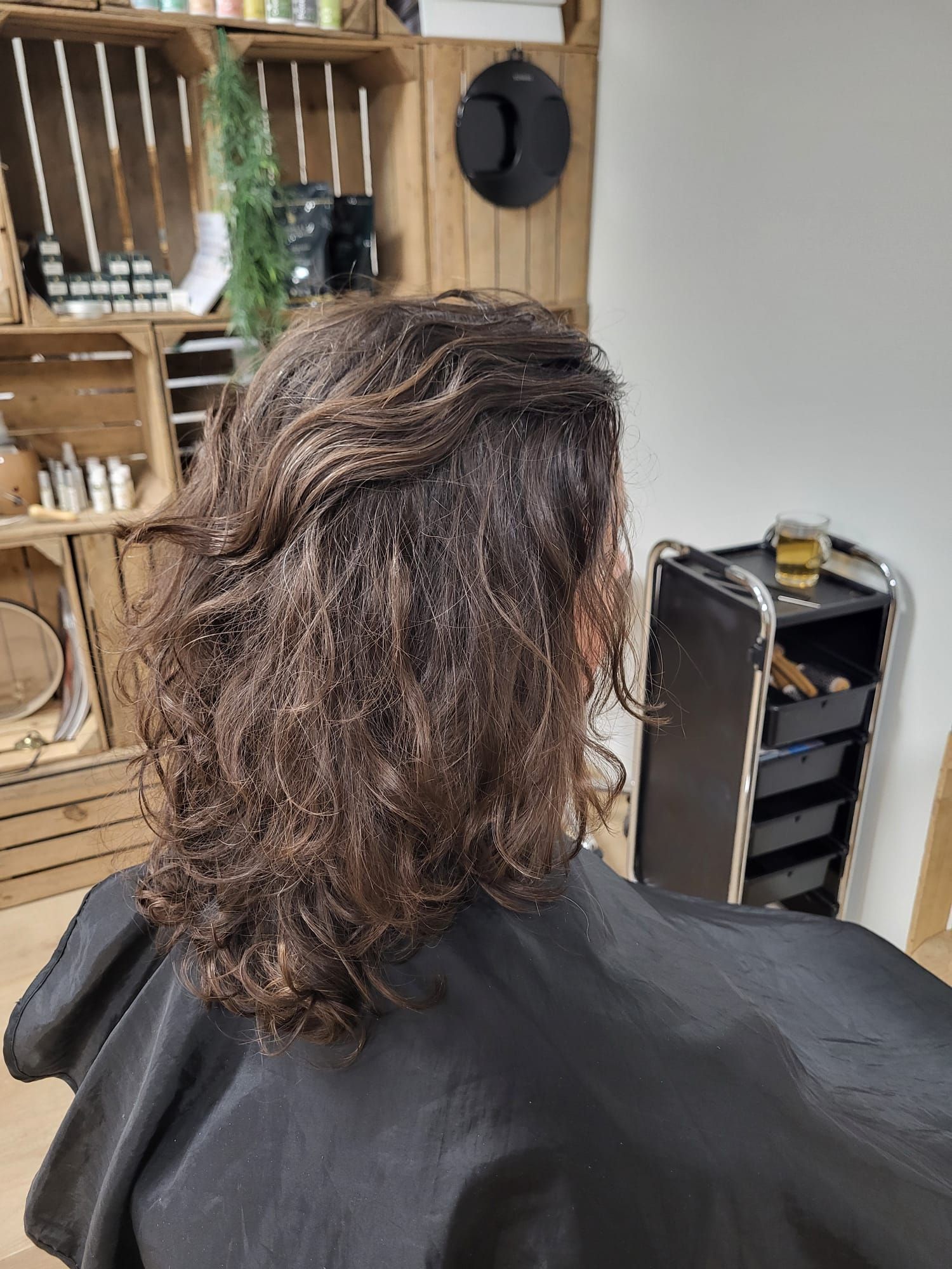 Persoon met schouderlang, golvend bruin haar in een kappersstoel, van achteren gefotografeerd tijdens een knipbeurt.