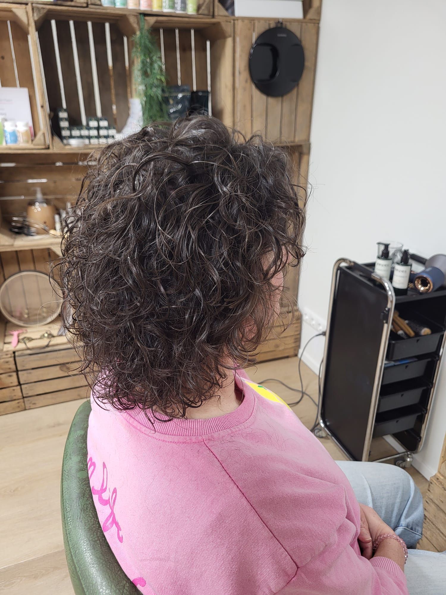 Persoon met krullend haar zit binnen in een roze top, van achteren gezien.