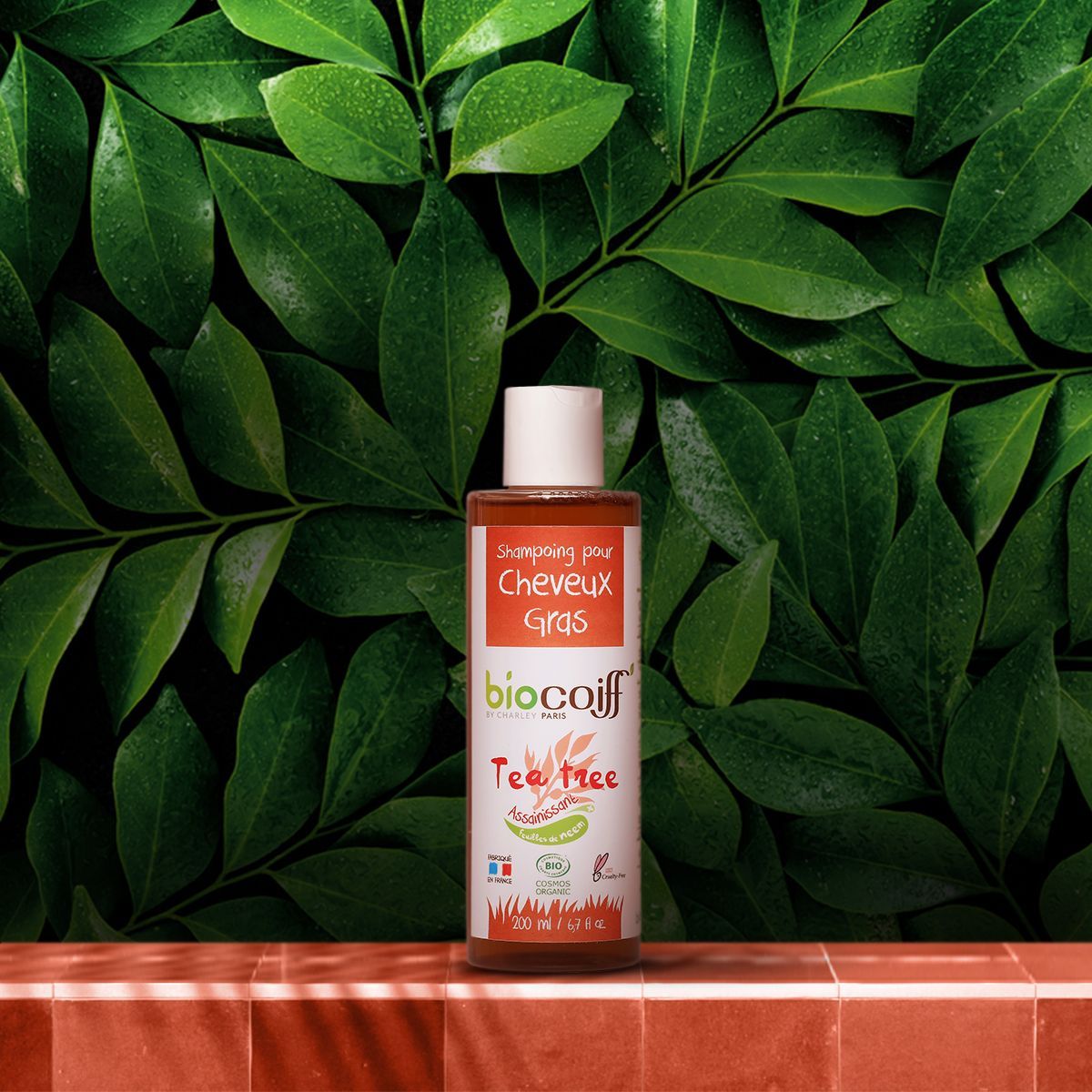 Witte fles haarproduct op een achtergrond van groene bladeren met een rode stoffen ondergrond.