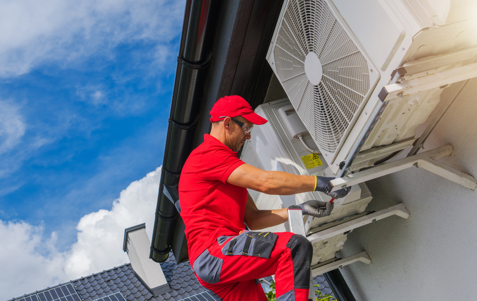 A man in a red shirt is installing an air conditioner on the side of a building.